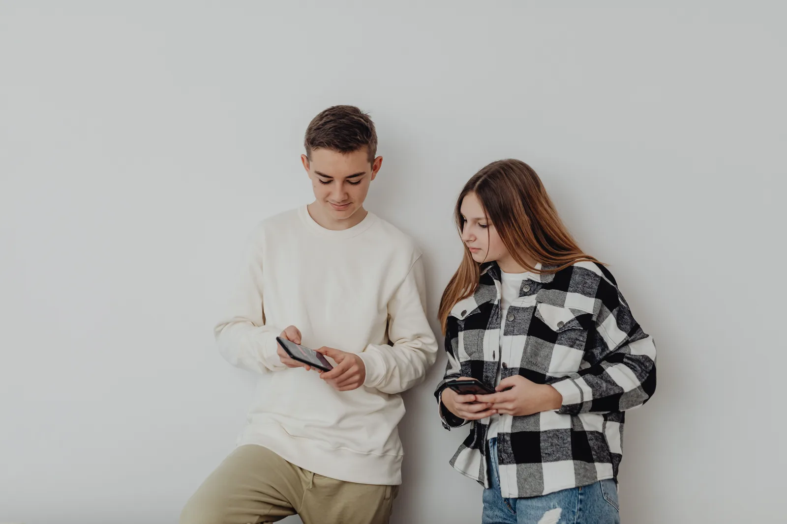 Teenage boy and girl using smartphones while leaning against a white wall indoors. How COPPA and California's design code change social apps for US teens