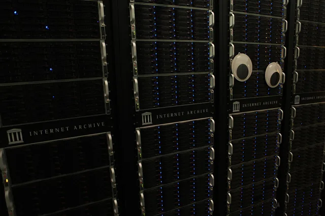 An isle of server racks in an Internet Archive data center, with large googly eyes on the front of one rack. The ethics and mechanics of archiving internet culture properly
